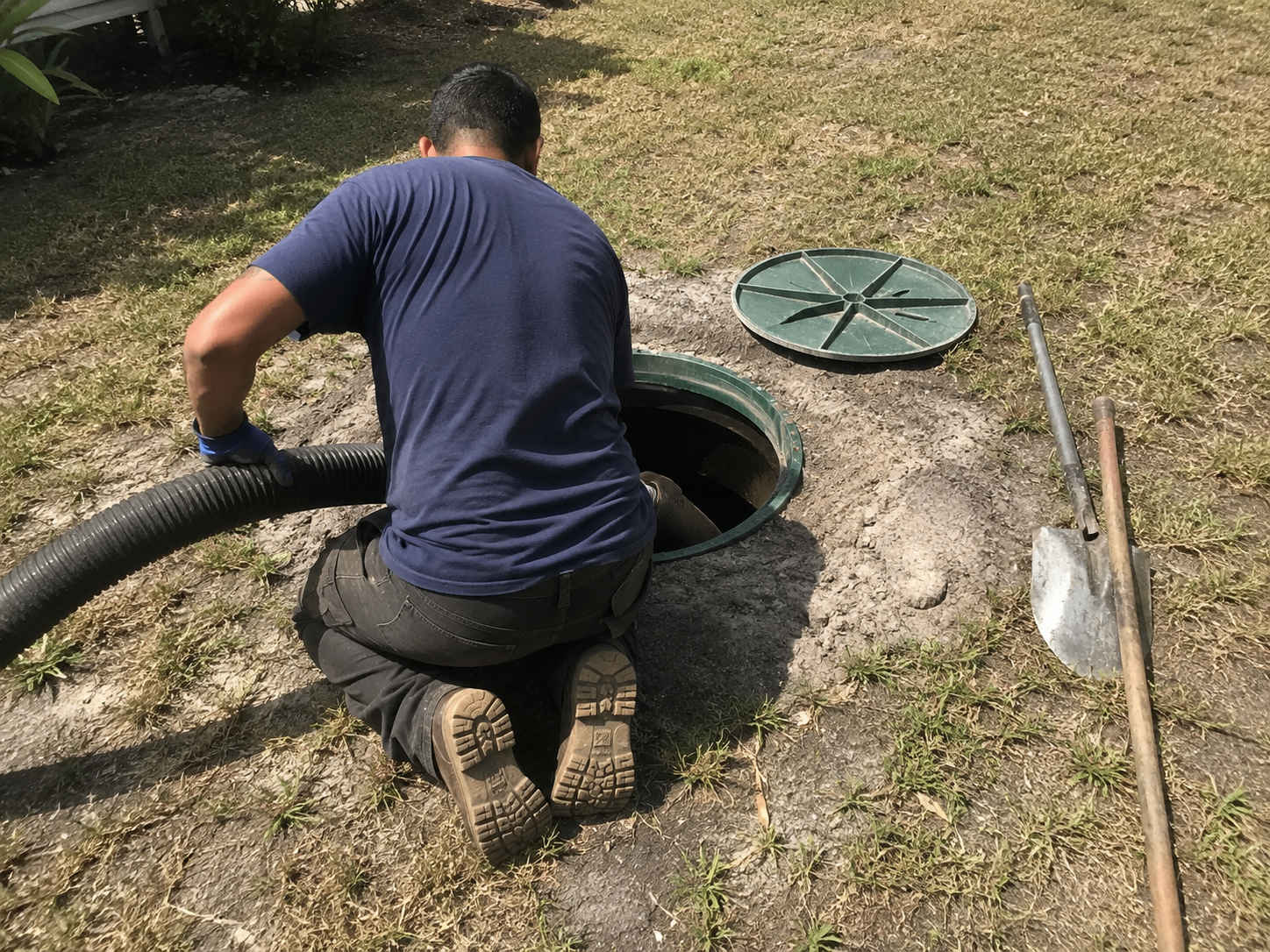 Operator lowering hose into open septic tank lid